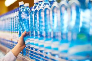 persona che prende una bottiglia di acqua dallo scaffale del supermercato