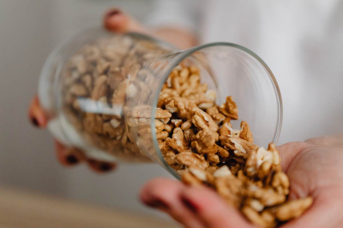 Persona che rovescia noci sgusciate dal contenitore alla mano