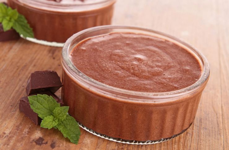 mousse al cioccolato dentro coppette di vetro e accanto delle foglioline di menta fresca