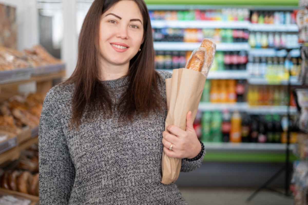 donna sorridente al supermercato che tiene in mano un sacchetto con dentro il pane