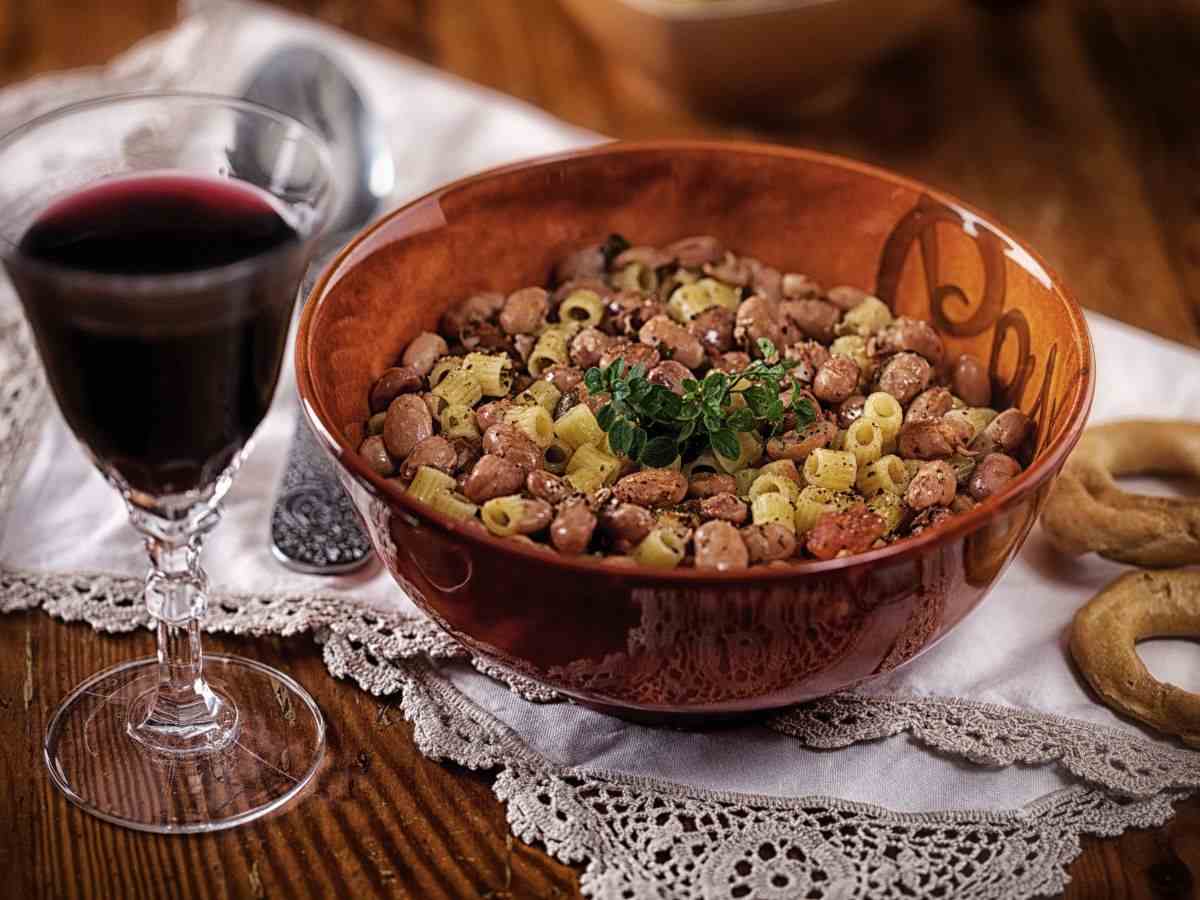 una ciotola con pasta e fagioli insieme a un calice di vino rosso