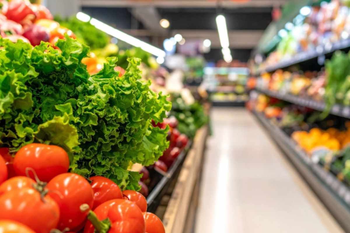 corsia del supermercato e in primo piano pomodori e insalata