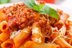 Piatto di penne al ragù con foglie di basilico e parmigiano