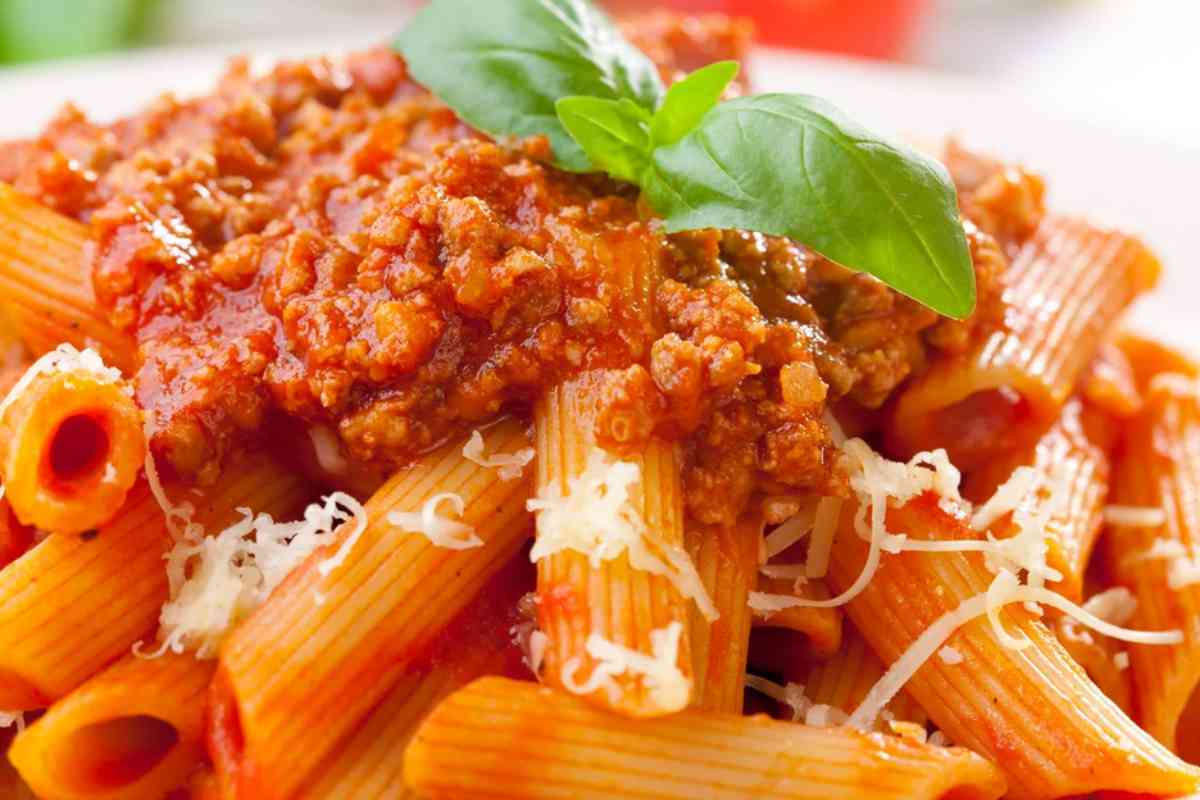 Piatto di penne al ragù con foglie di basilico e parmigiano