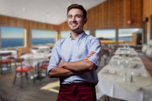 Cameriere con le braccia incrociate in primo piano e ristorante sullo sfondo