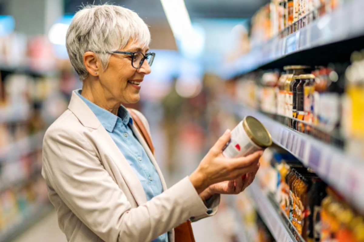 donna anziana al supermercato con in mano un barattolo