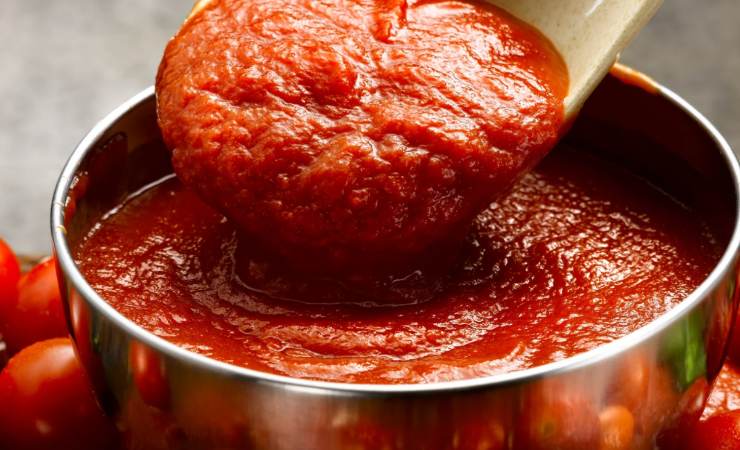 Sugo di pomodoro in una pentola prelevato con mestolo