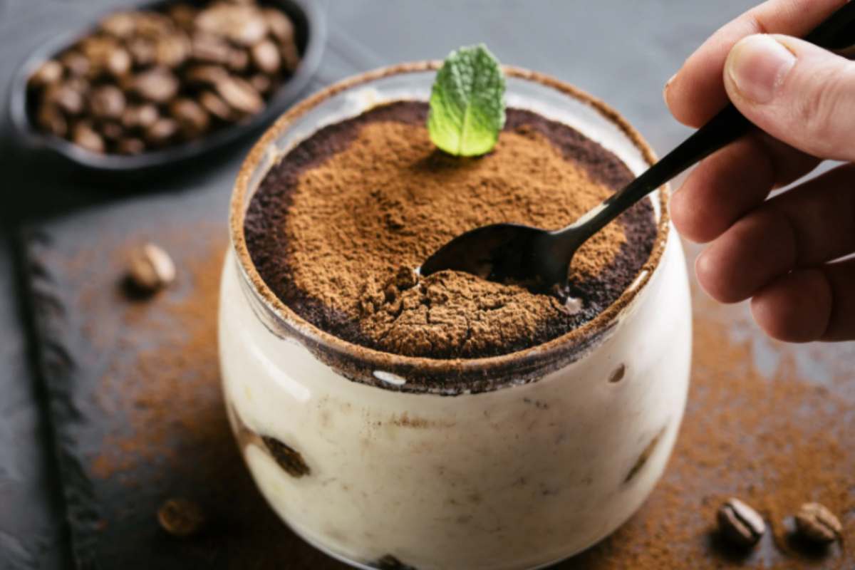 persona che affonda un cucchiaino in un bicchiere di tiramisù