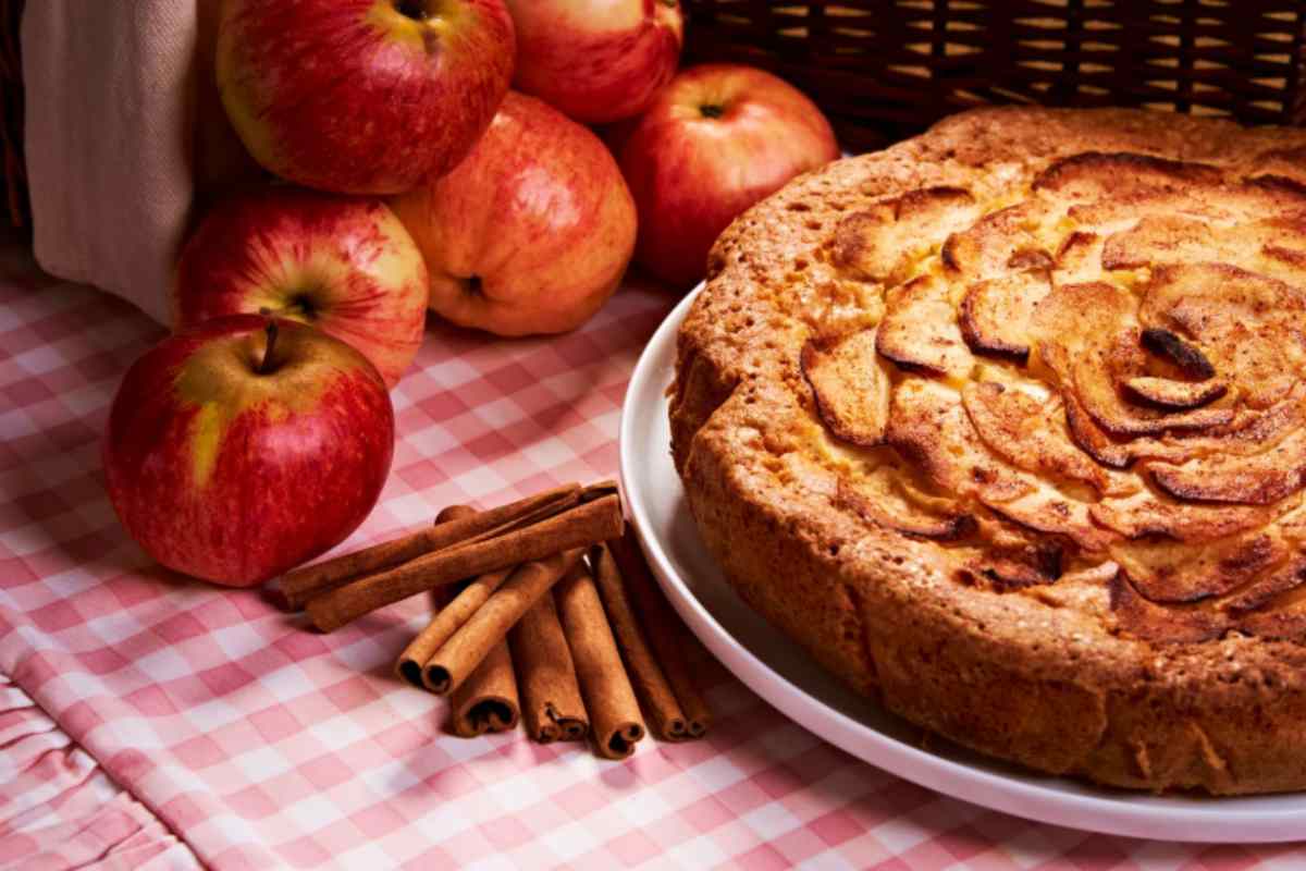 torta di mele con accanto delle mele rosse e della cannella